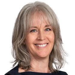 Smiling woman with shoulder-length gray hair and bangs, wearing a dark top, is pictured against a plain white background—reflecting the diverse community found on an urban campus in Toronto.