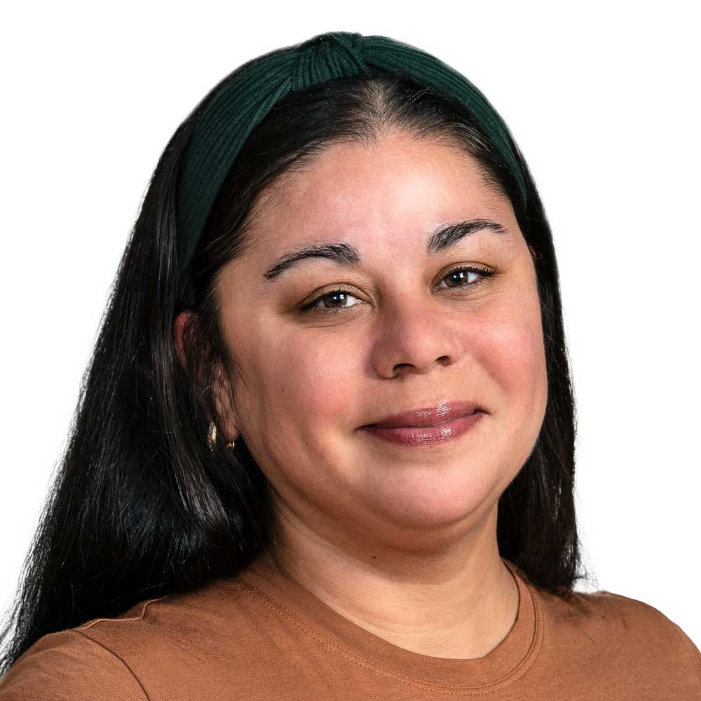 A woman with long dark hair, wearing a green headband and brown top, smiles softly at the camera against a plain white background.