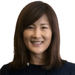 A woman with straight, shoulder-length brown hair, wearing a dark top, smiles at the camera against a plain white background—reflecting her passion for global education for girls.