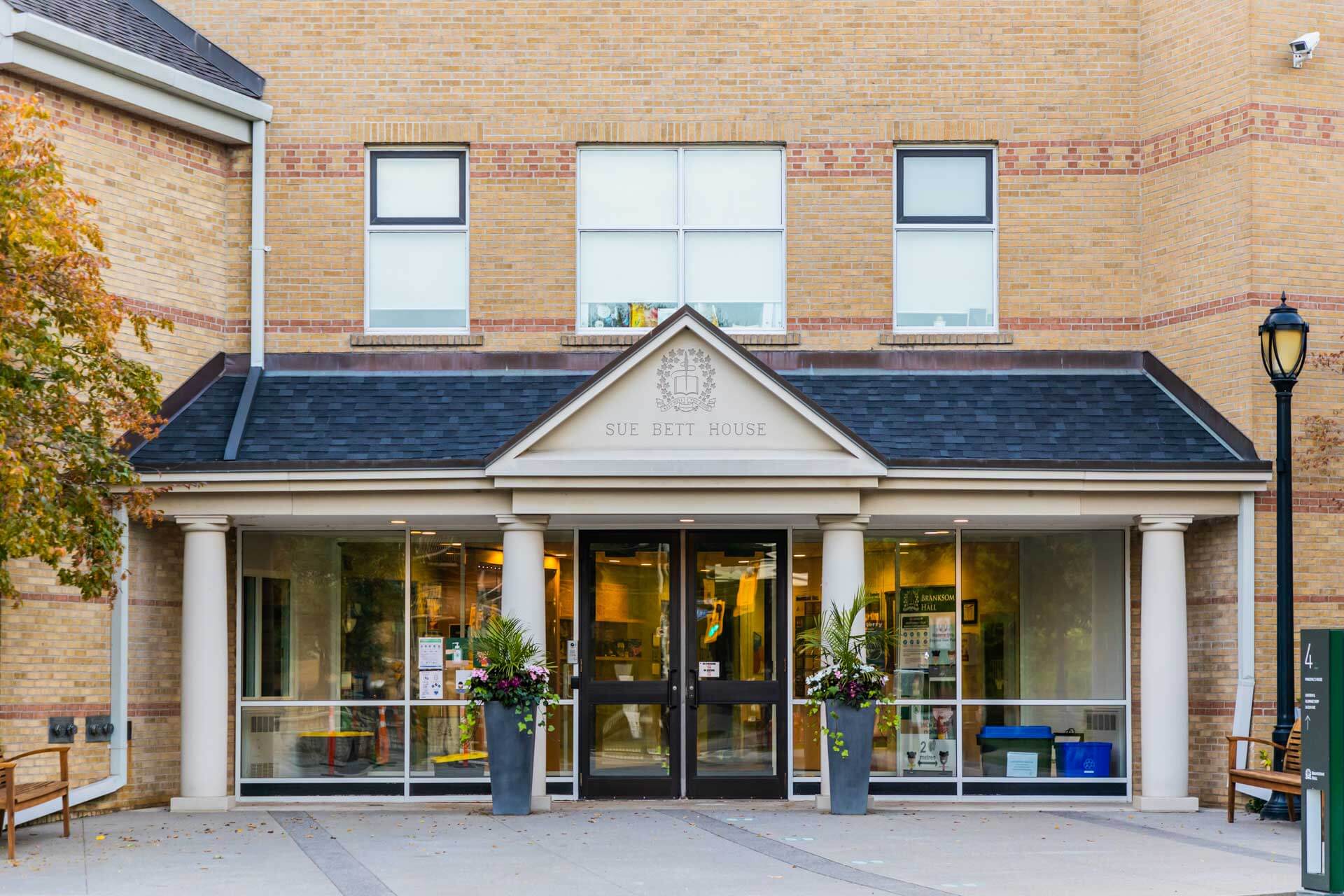 The entrance of "Sue Bett House"—with glass doors, tall windows, potted plants, and white columns—welcomes students to a space dedicated to Global education for girls and the renowned IB Diploma Programme.