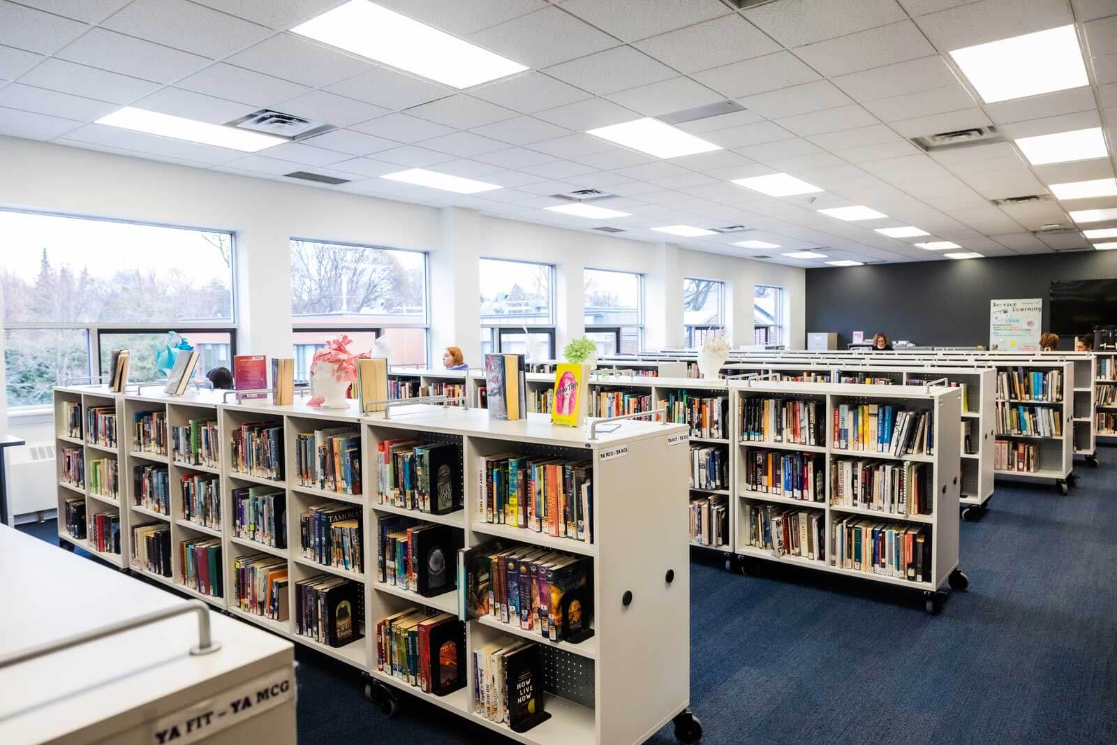Rows of bookshelves filled with books in a bright, modern library create an inviting space on our urban campus in Toronto. Large windows provide natural light, making it the ideal spot for girls pursuing global education or the IB Diploma Programme.