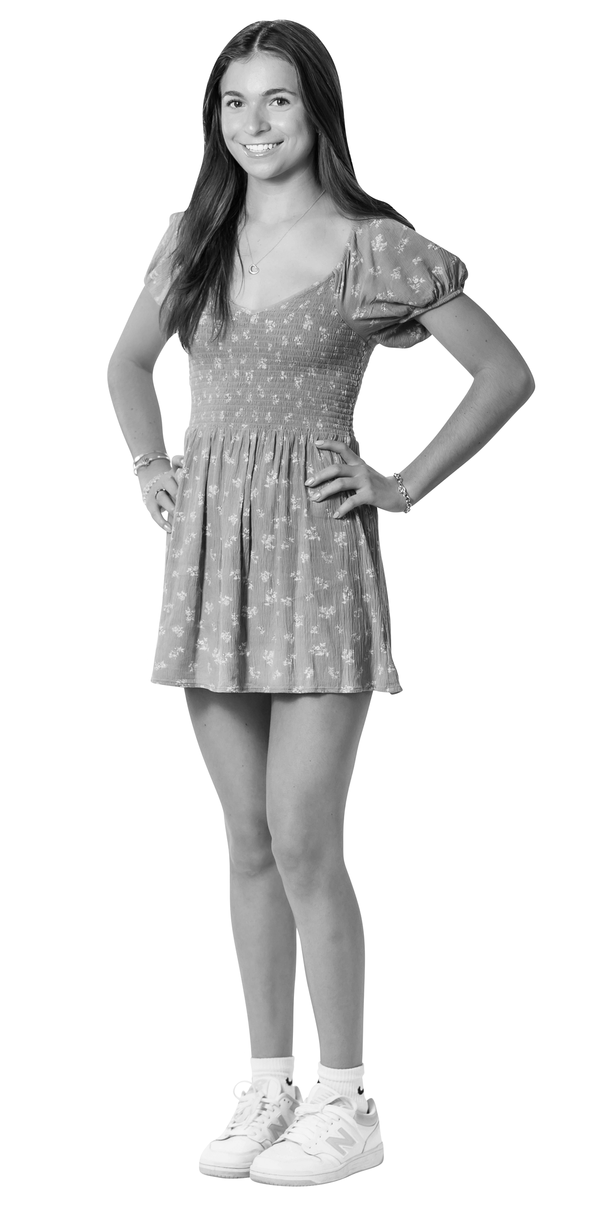 A young woman stands smiling with hands on her hips, wearing a short-sleeved, patterned dress and white sneakers. She has long, straight hair and appears confident. The image is in black and white with a white outline.