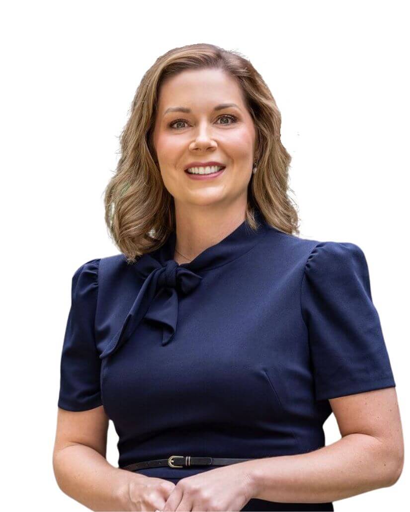 A woman with shoulder-length light brown hair, wearing a navy blue dress with short sleeves and a bow at the collar, smiles while standing against a white background.
