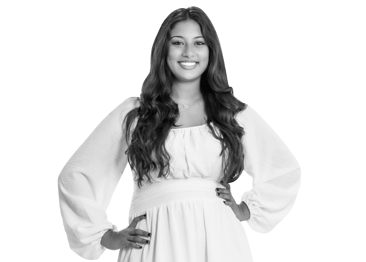 A young woman with long, wavy hair smiles confidently at the camera. She is wearing a white, long-sleeved dress and has her hands on her hips. The background is white, creating a clean and bright portrait.