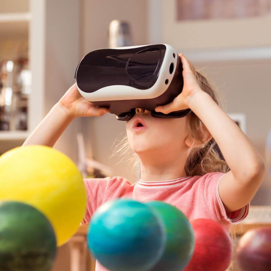 A young child wearing a virtual reality headset looks up in wonder, surrounded by colorful model planets, suggesting an immersive learning experience about space.