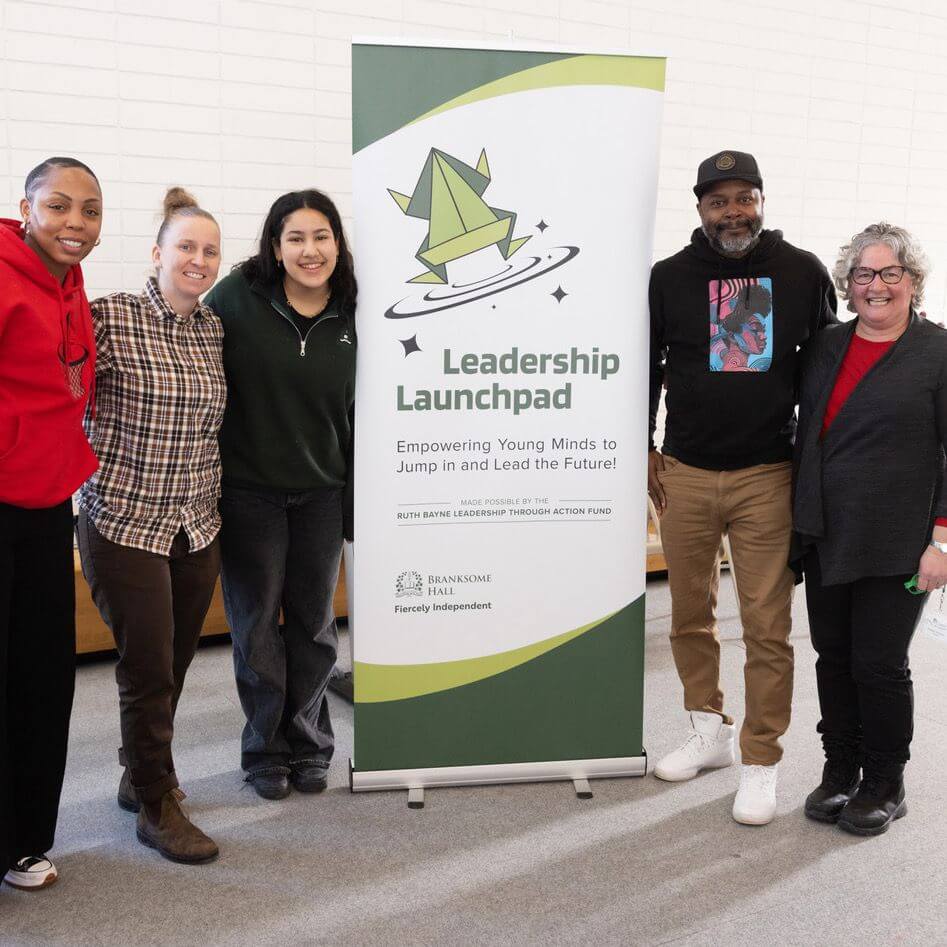 Five people stand smiling around a "Leadership Launchpad" banner, which reads: "Empowering Young Minds to Jump in and Lead the Future!" The group appears friendly and diverse in a bright indoor setting.