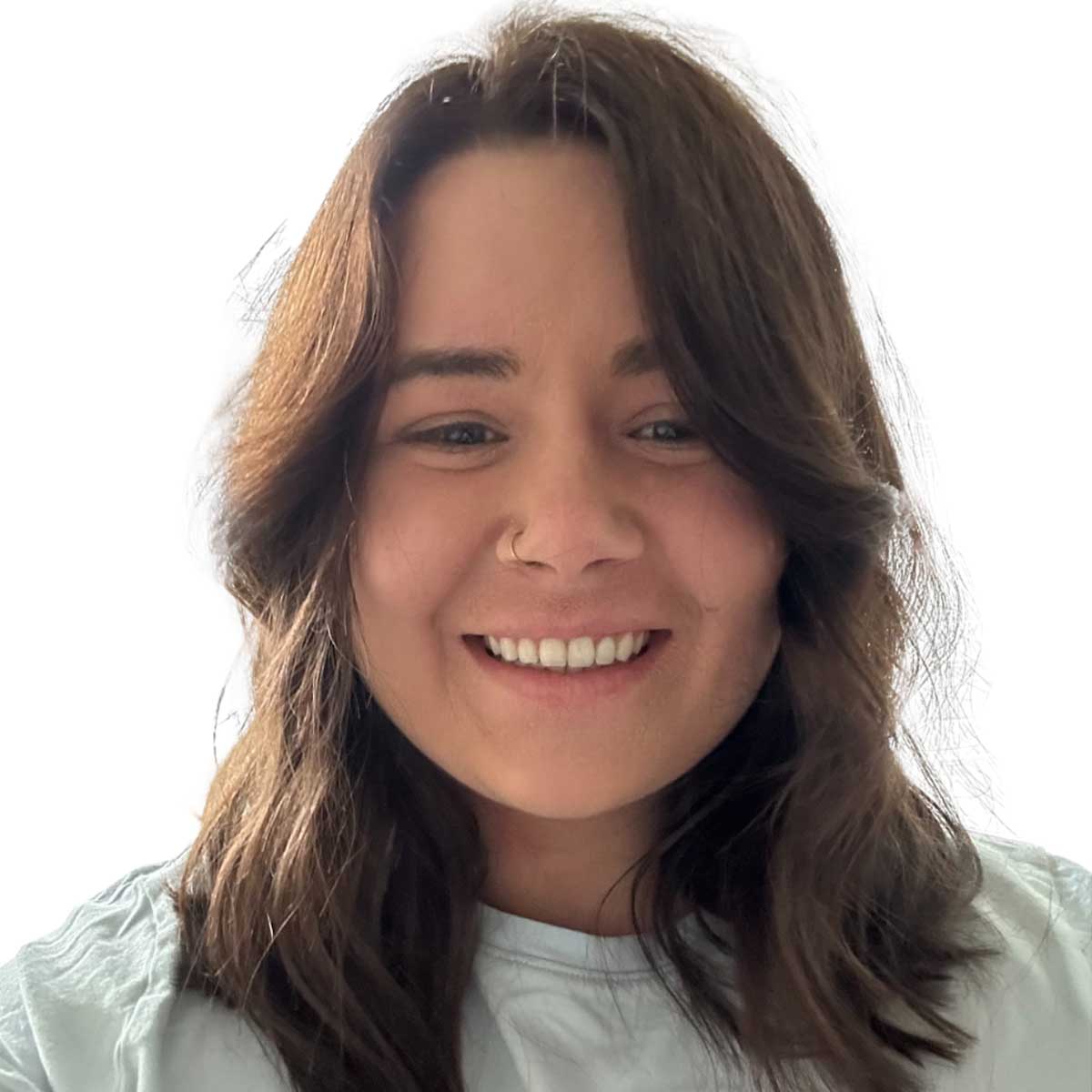 A woman with shoulder-length brown hair and a nose ring smiles at the camera. She is wearing a light-colored shirt and is photographed against a plain white background.