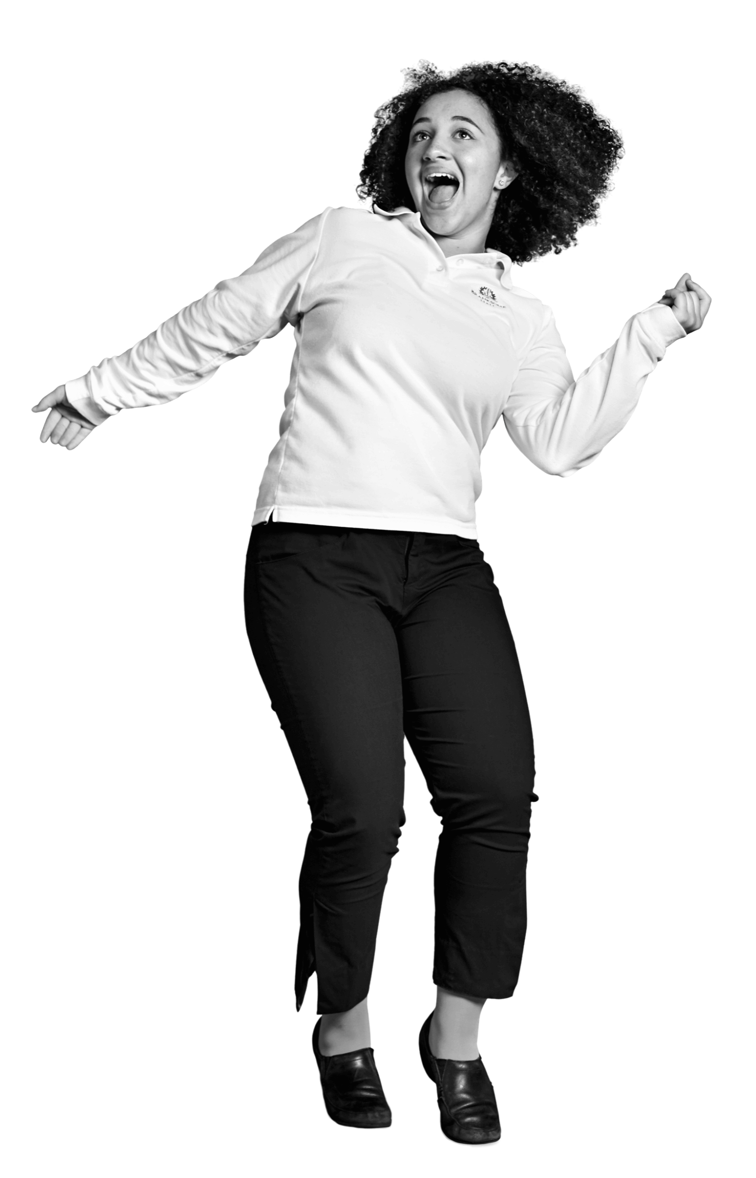 A woman with curly hair, wearing a white long-sleeve shirt and dark pants, is jumping joyfully with a wide smile, arms outstretched, and looking upward.