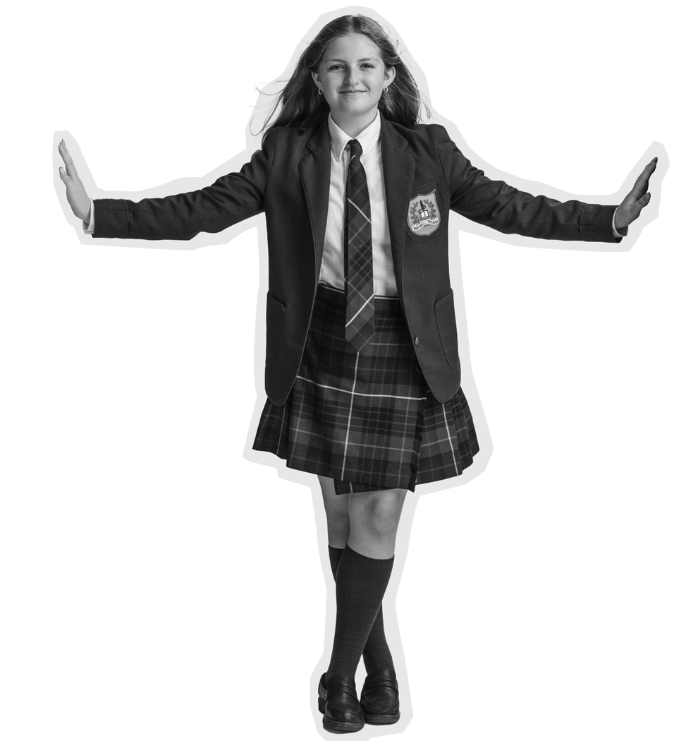 A girl in a school uniform with a plaid skirt, blazer, and tie stands with her arms outstretched, smiling. She is wearing knee-high socks and loafers. The background is plain and light-colored.