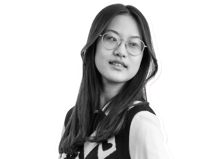 A young woman with long dark hair and glasses looks slightly to the side. She is wearing a patterned sweater vest over a collared shirt. The image is in black and white with a white outline around her.