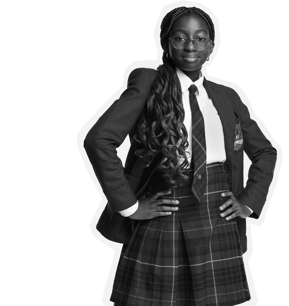 A confident student wearing glasses, a school uniform with a plaid skirt, blazer, and tie stands with hands on hips, looking forward and smiling slightly.