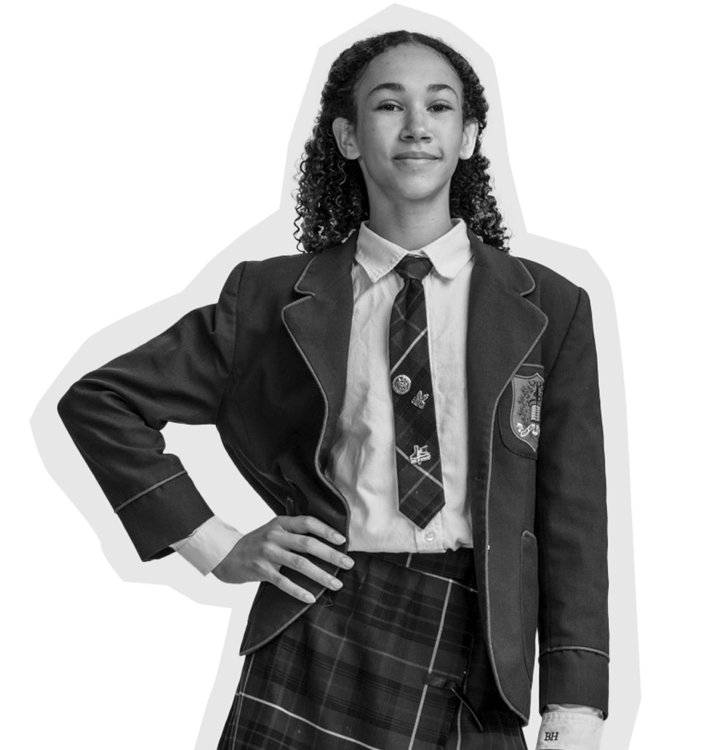 A young student with curly hair stands confidently, wearing a school uniform with a blazer, tie, and plaid skirt, and has one hand on her hip. The image is in black and white.