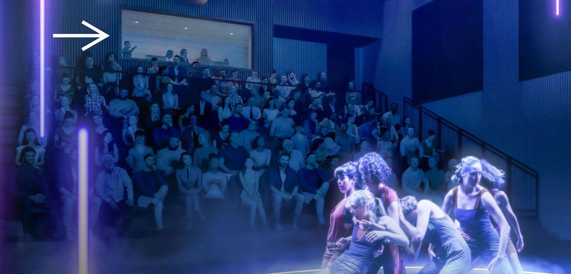 A group of four dancers performs on a stage with blue lighting, while a large audience watches from tiered seating; an arrow points to people observing from a windowed booth above the crowd.