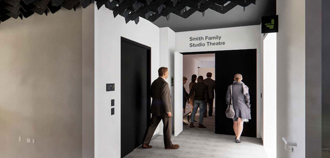 Several people walk through a hallway toward the entrance of the Smith Family Studio Theatre. One man in a suit is approaching double doors, and others are visible inside the well-lit space.