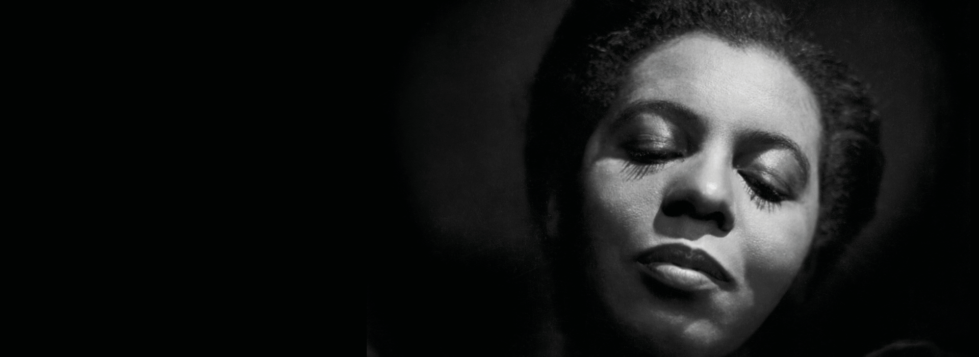 Black and white close-up of a woman with short hair and closed eyes, her expression calm and serene, set against a dark background.