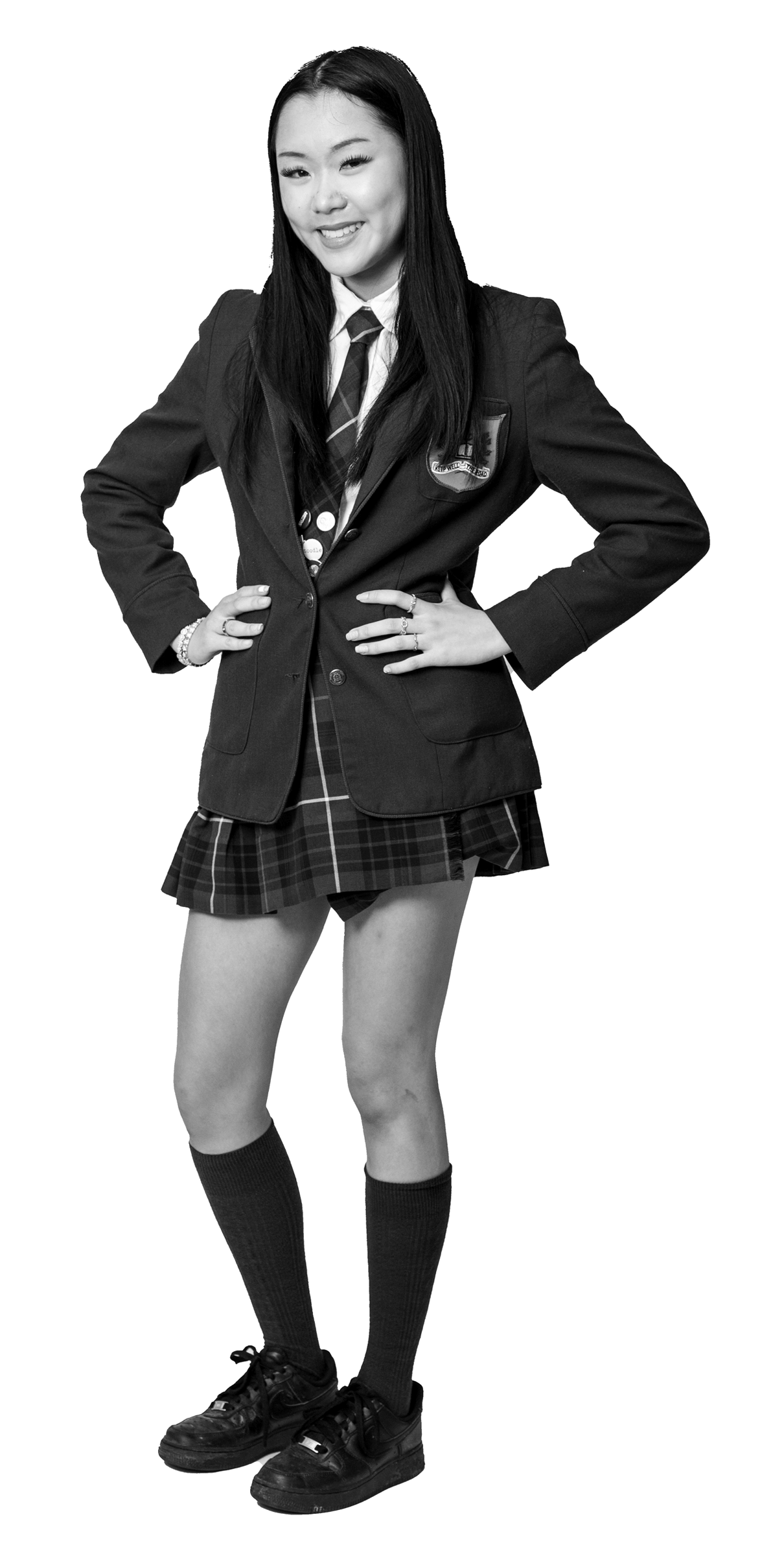 A young woman wearing a school uniform with a blazer, tie, plaid skirt, knee-high socks, and sneakers stands smiling with her hands on her hips. The image is in black and white with a white outline around her.