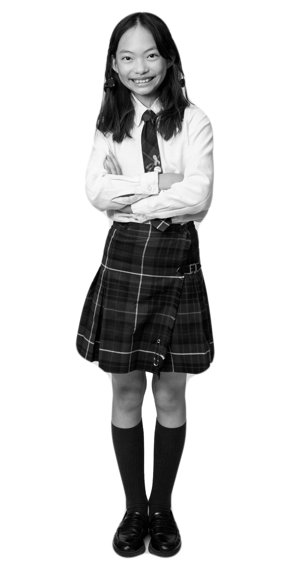 A girl wearing a school uniform with a plaid skirt, necktie, long-sleeved shirt, knee-high socks, and loafers stands smiling with arms crossed.