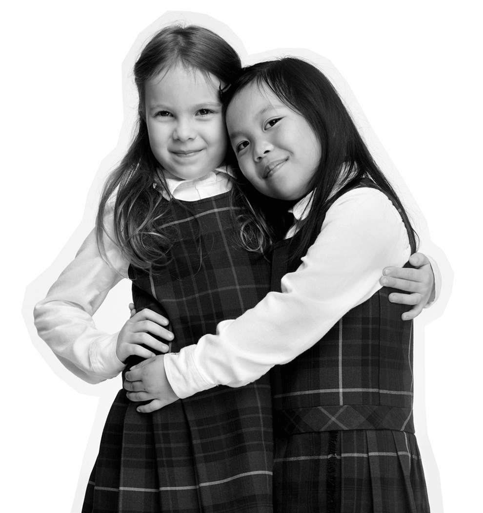 Two young girls in school uniforms hug each other and smile, standing close together. The image is in black and white with a white outline around them.