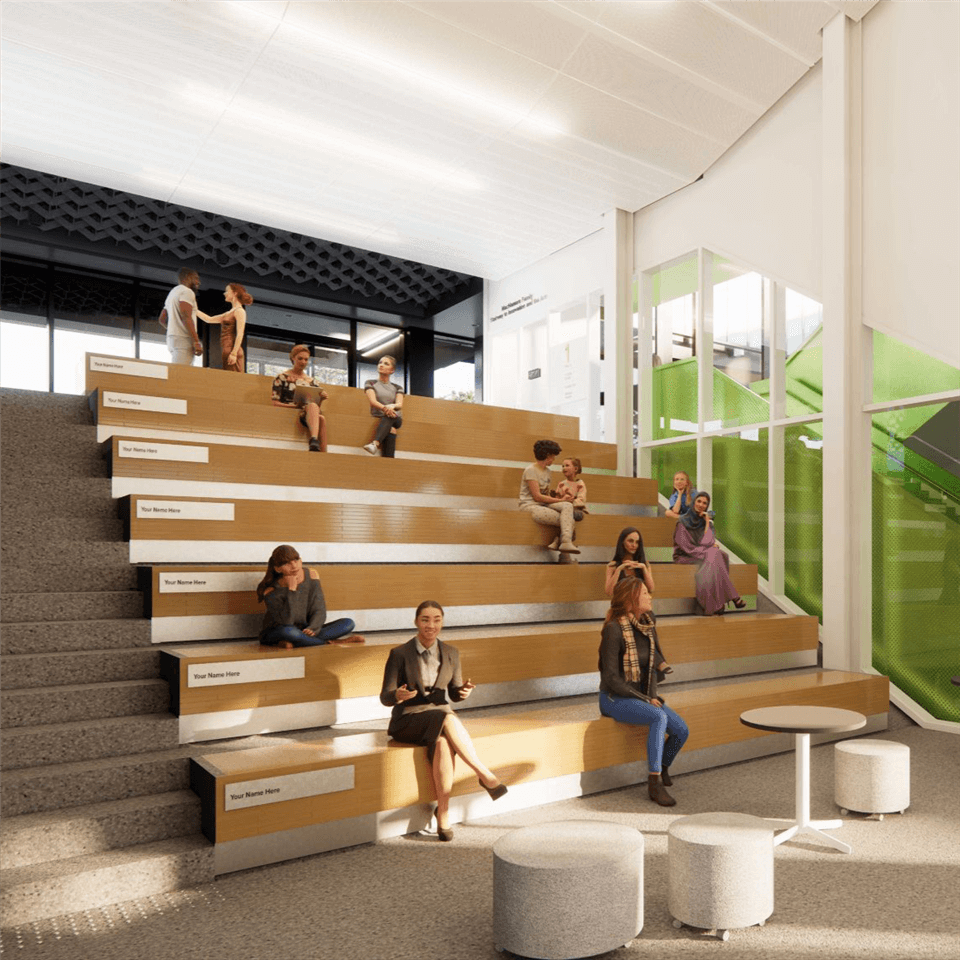 A modern, open stair seating area with people sitting and talking. The space has large windows, a green staircase, and round ottomans with small tables in the foreground. Natural light fills the bright, airy environment.